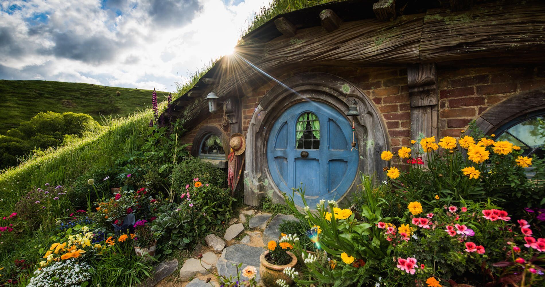 Uma pequena casa de tijolos com uma porta azul é cercada por flores.