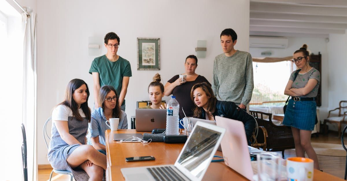 Um grupo de pessoas está sentado ao redor de uma mesa com laptops.