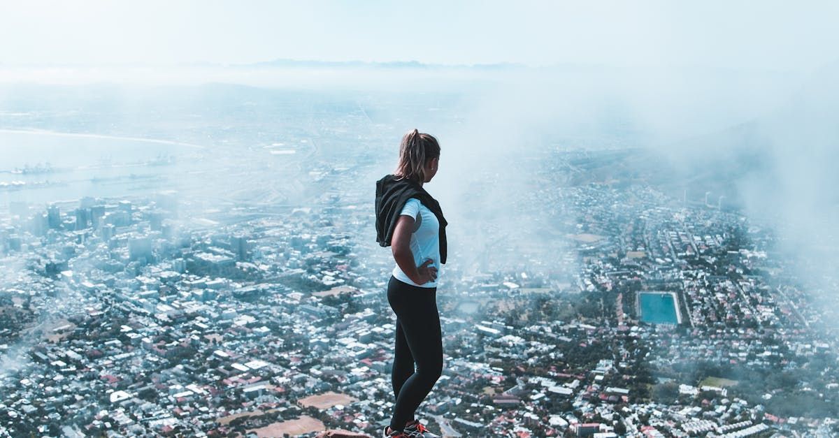 Uma mulher está no topo de uma montanha com vista para uma cidade.