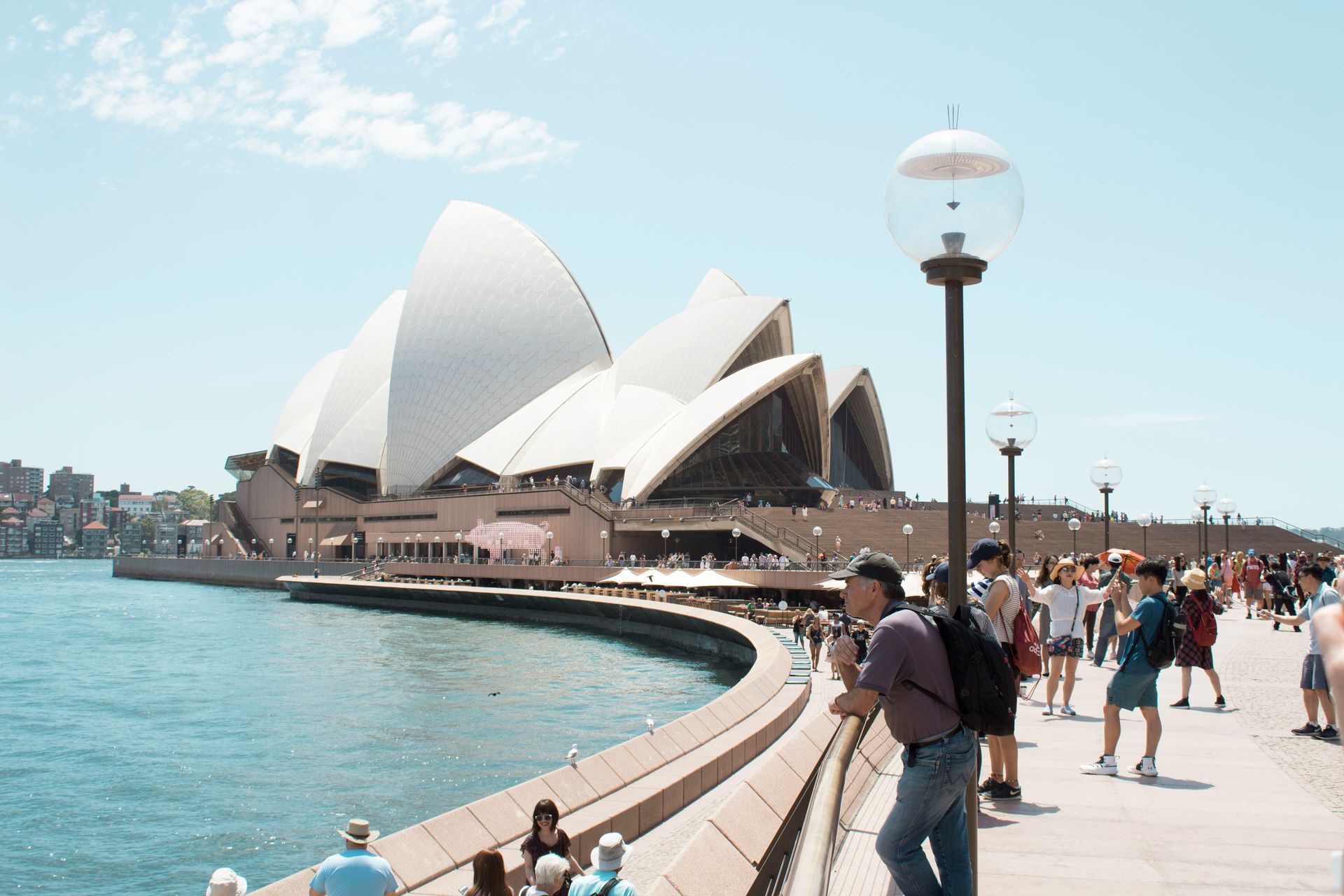 Um grupo de pessoas está parado na calçada em frente à Ópera de Sydney.