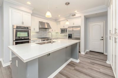 Modern white kitchen with stainless steel appliances, gray island, and light wood floors.
