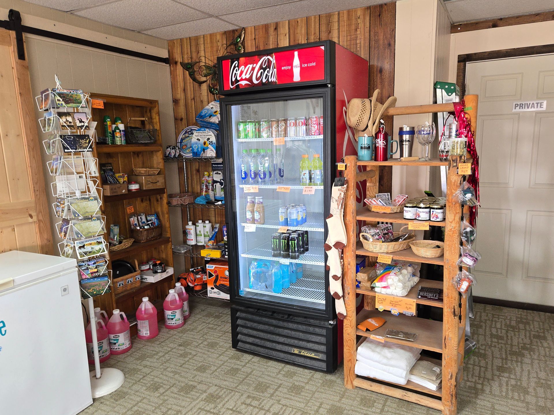 A small store interior with shelves and a refrigerator, selling drinks and various items.