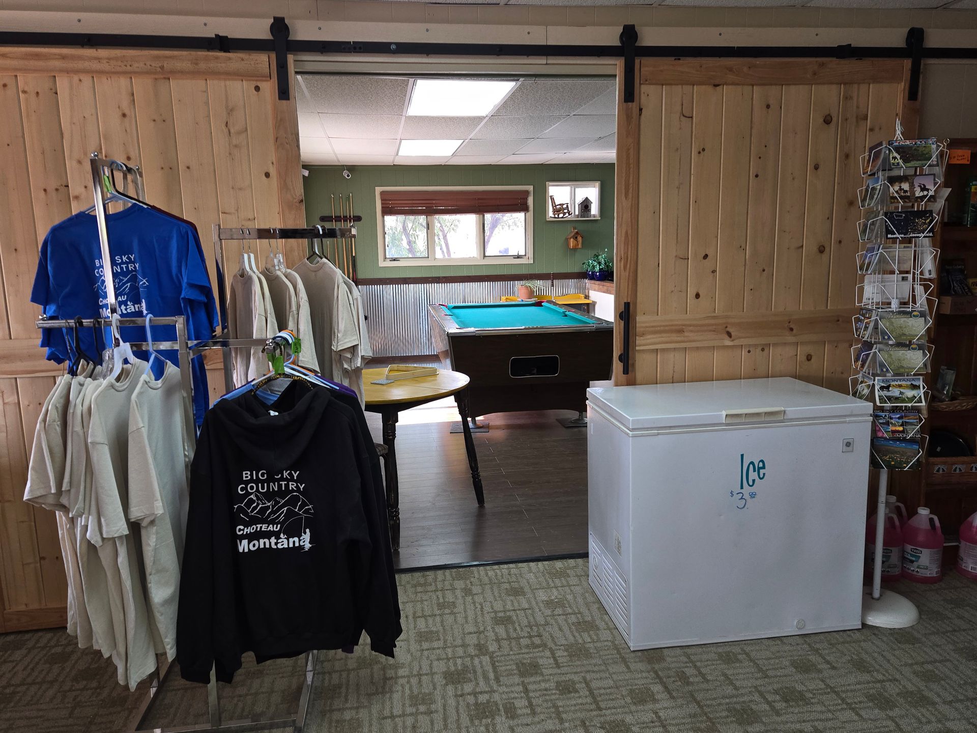 Clothing racks, freezer, and open doorway to a room with a pool table and window.