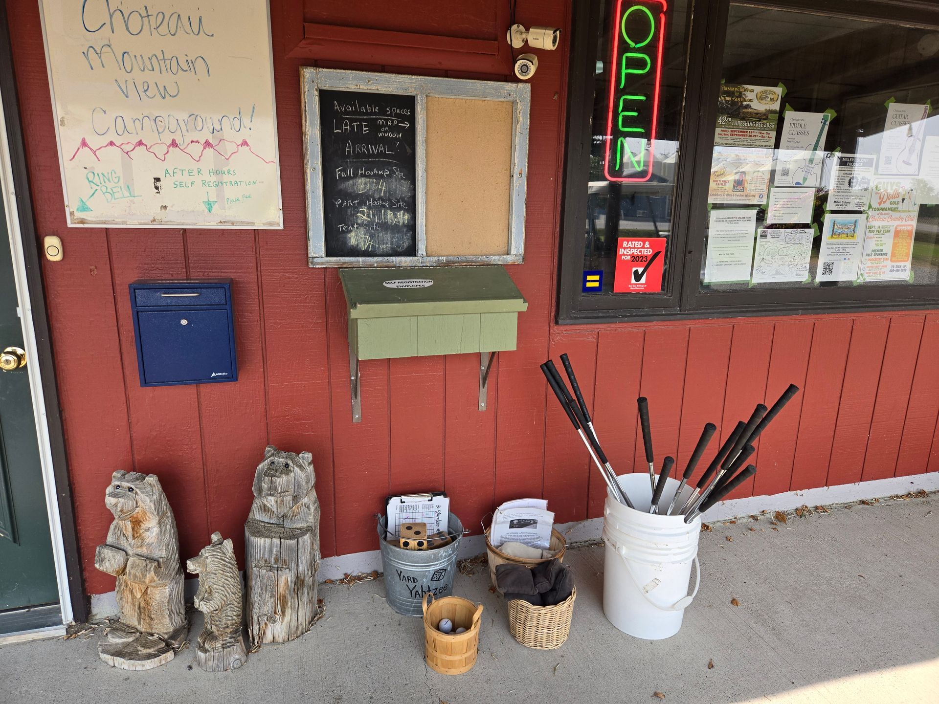 Exterior of a shop with a red wall and items for sale, including wooden bear carvings and golf clubs.