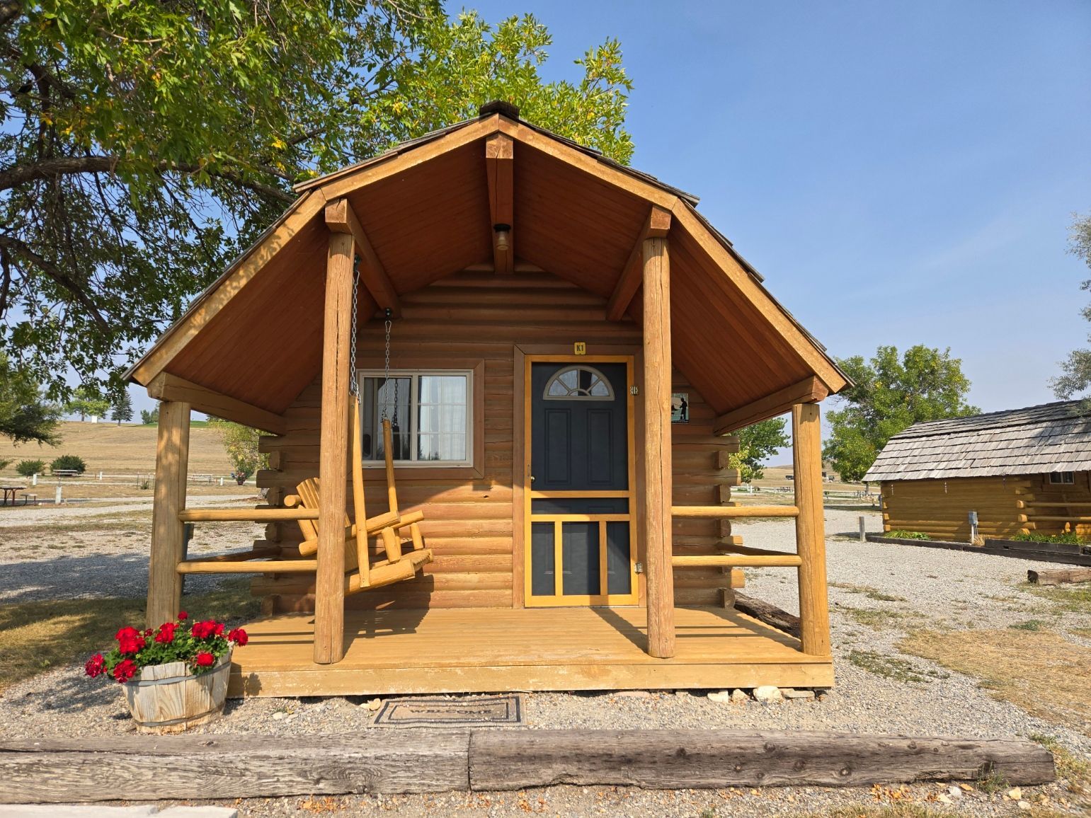 Small wooden cabin with porch, swing, and flower pot. Blue door and screen door.