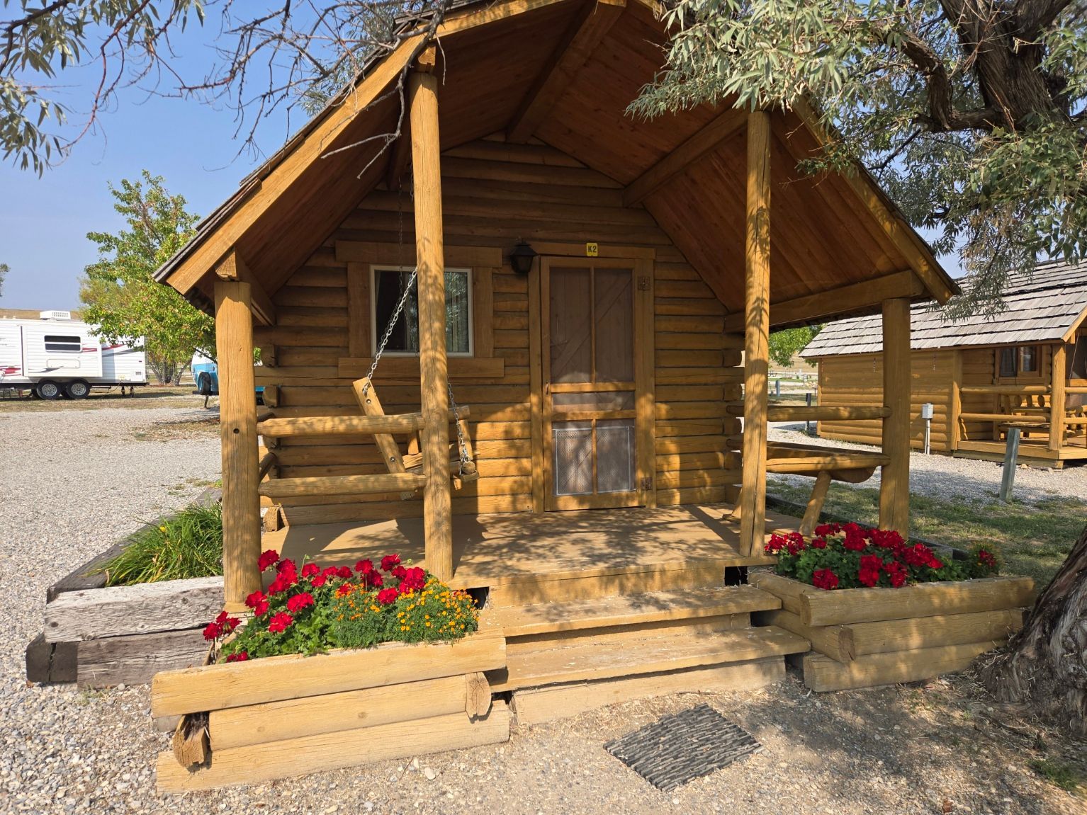 Wooden cabin with porch, flower boxes, and picnic table in a campground setting.