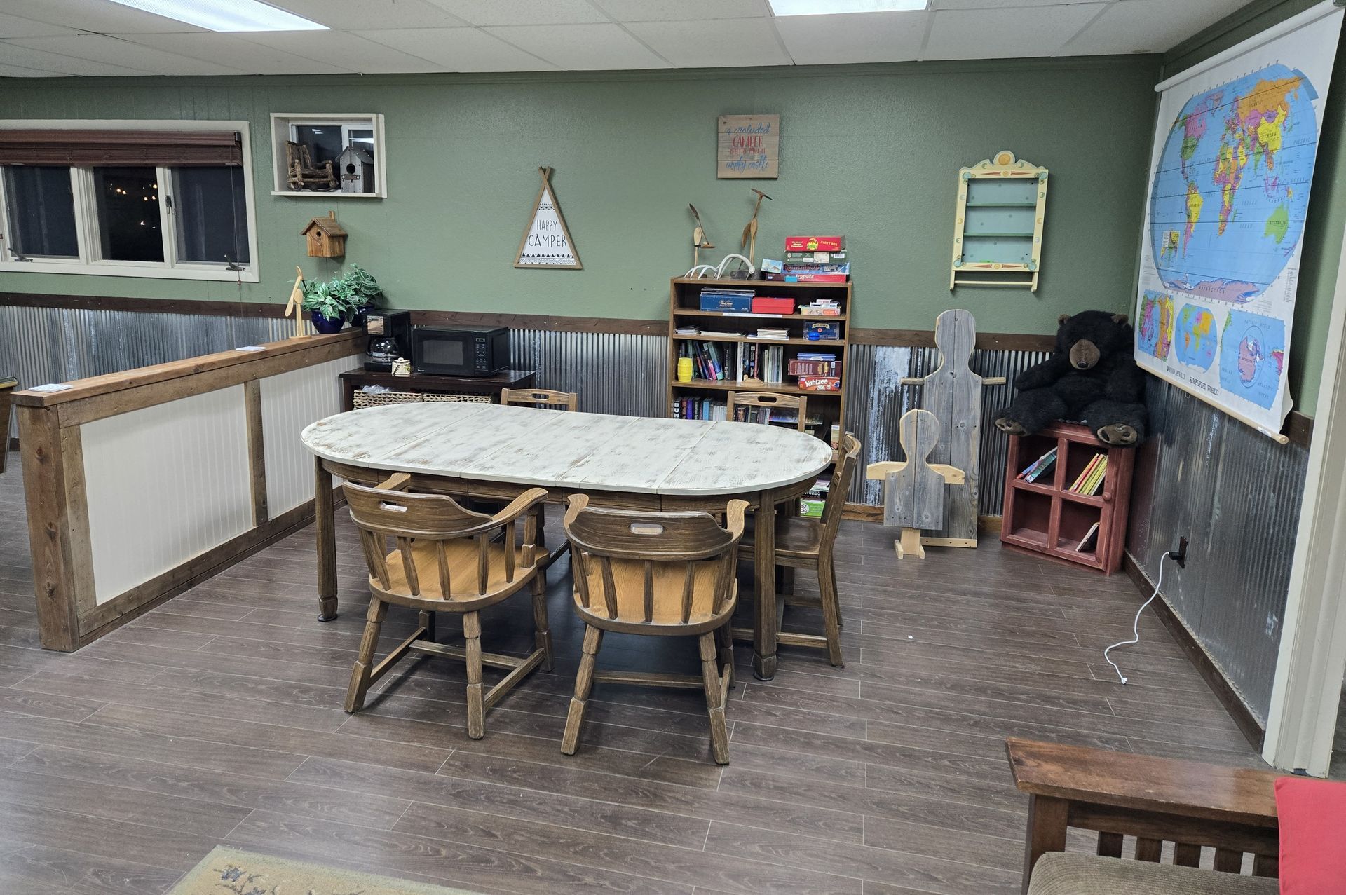 Room with oval table, chairs, books, a world map, and various decorations on green and metal walls.