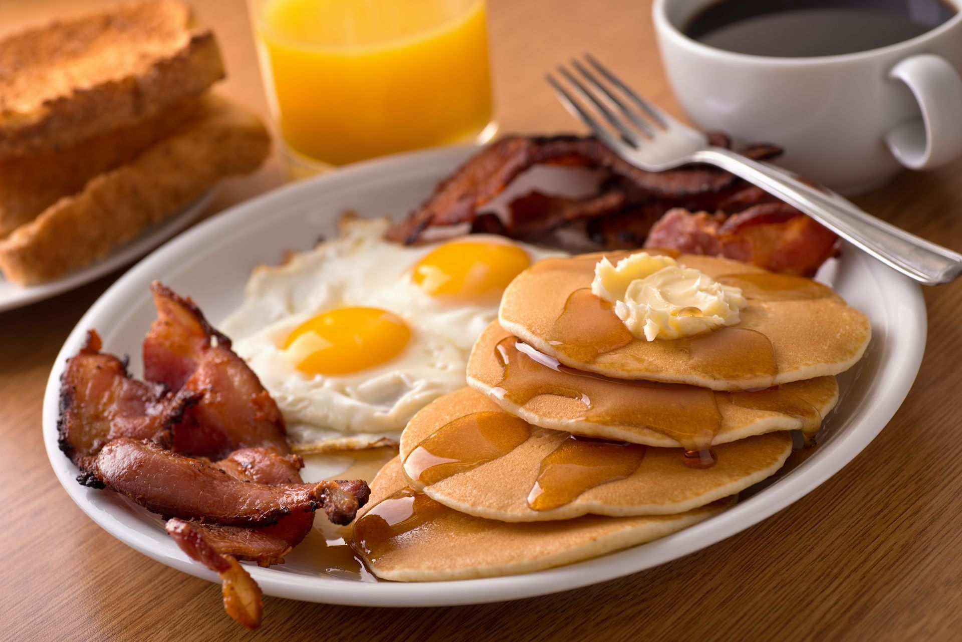 Breakfast plate with pancakes, eggs, bacon, toast, coffee, and orange juice.