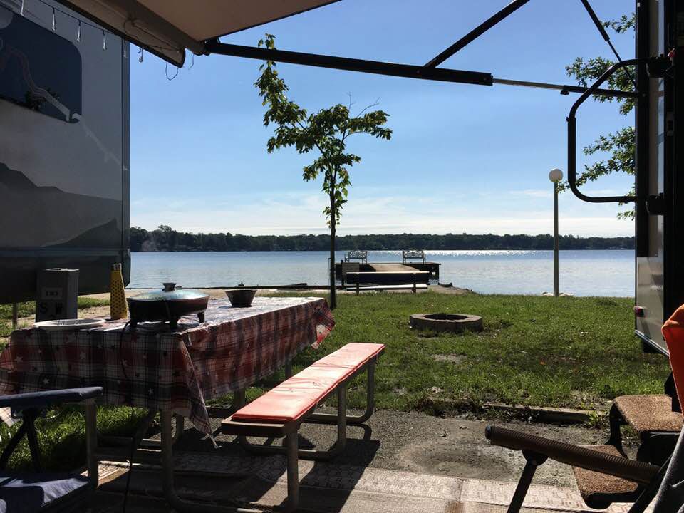 Lakeside patio with picnic tables, canopy shade, and a small tree by the water