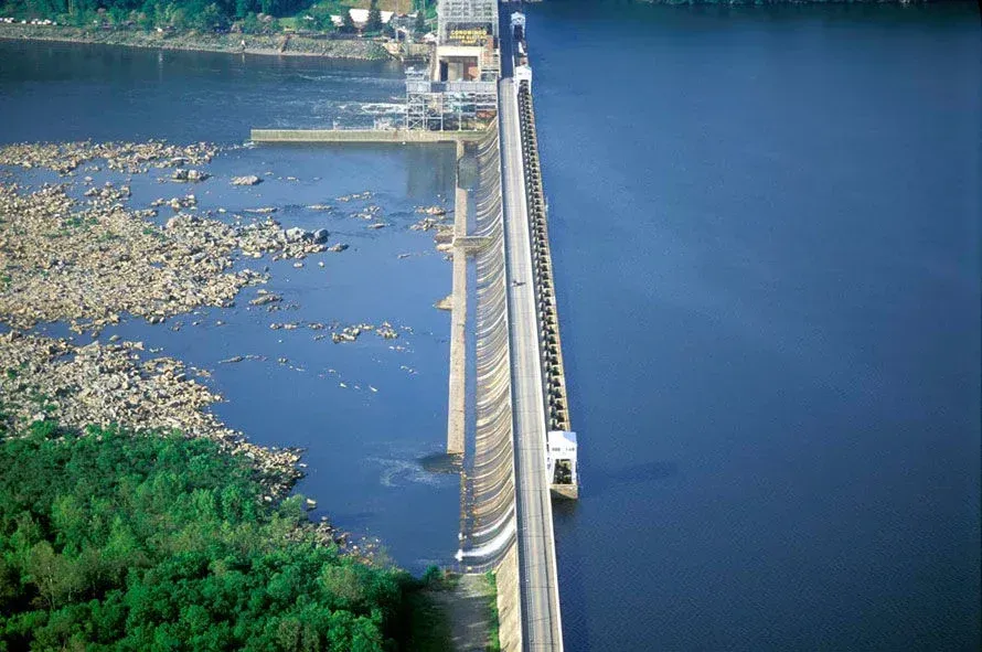 A dam separates rocky river water on the left from deep blue reservoir water on the right.