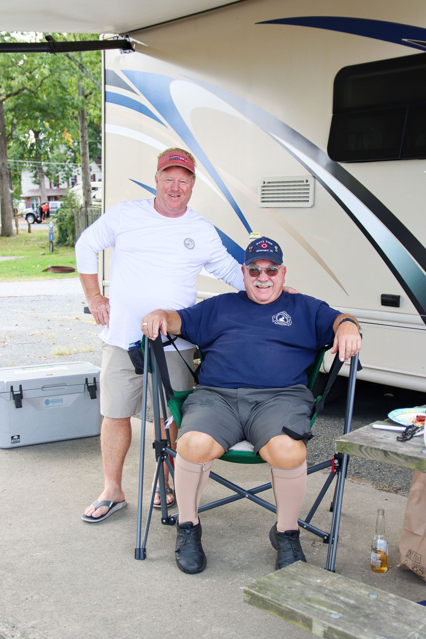 Two men outside an RV, one seated in a wheelchair and one standing beside him.
