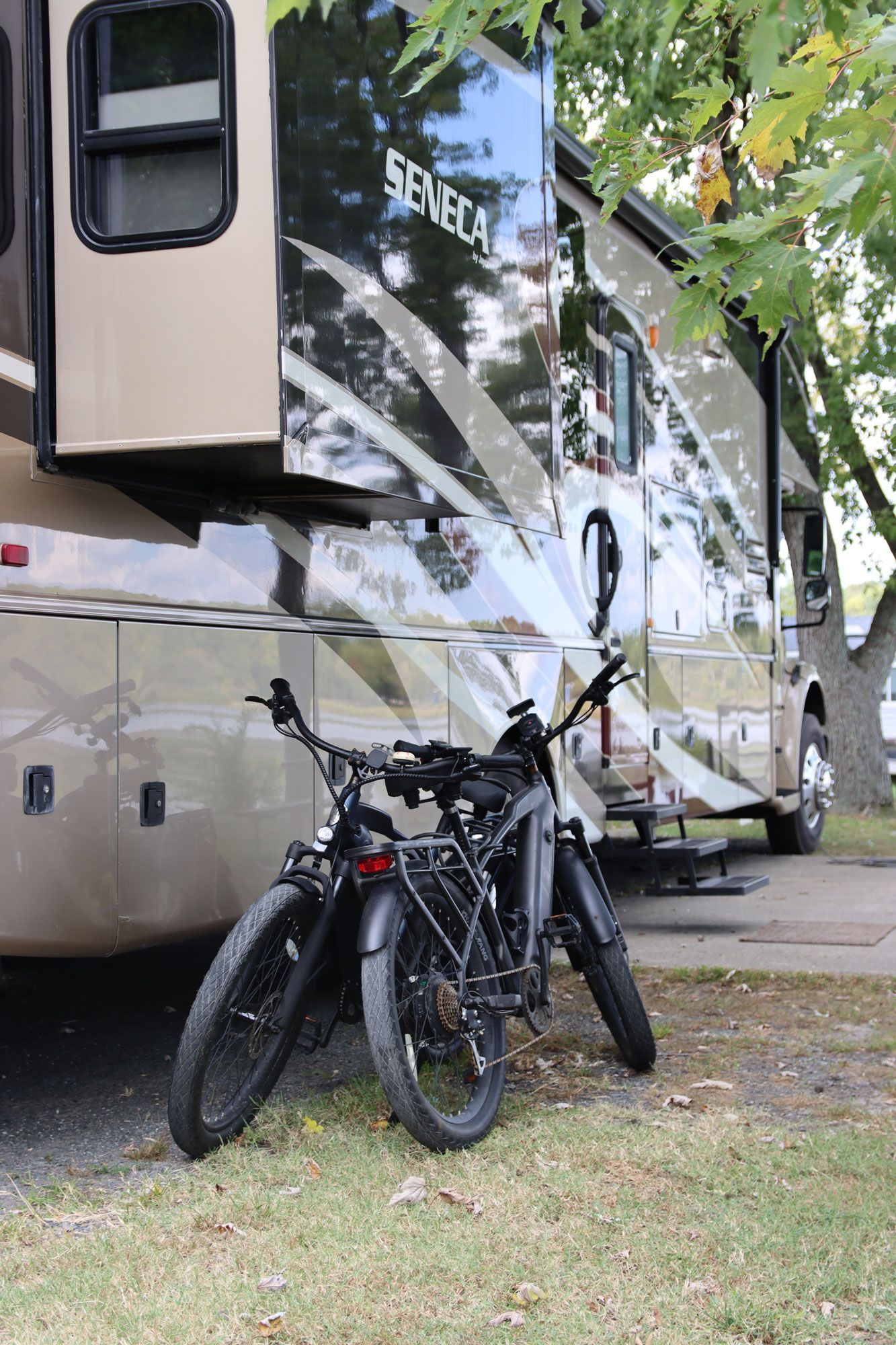 Two black bicycles parked beside a tan RV under trees on grass