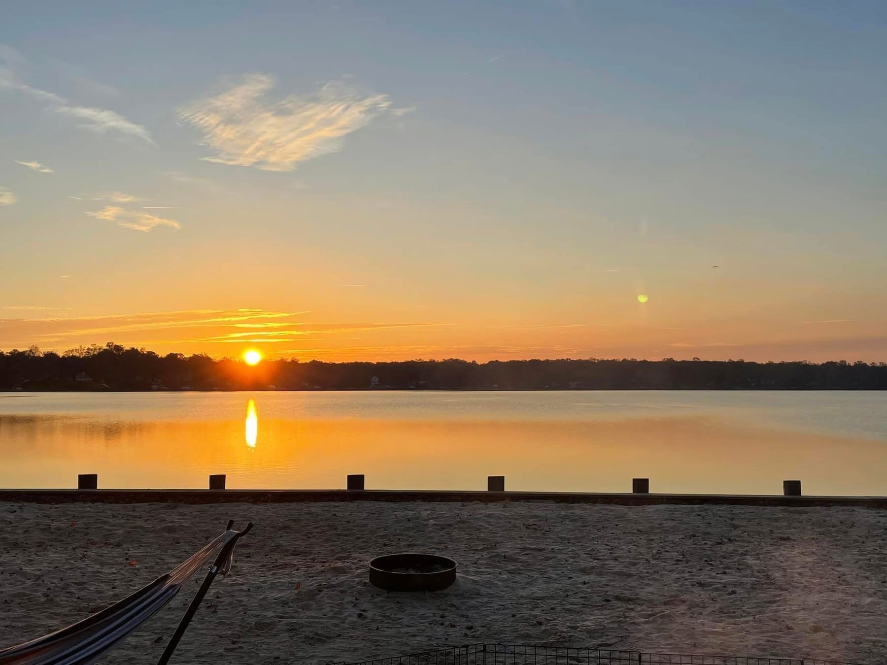 Sunset over a calm lake, with orange reflection on the water and a silhouetted shoreline in the distance