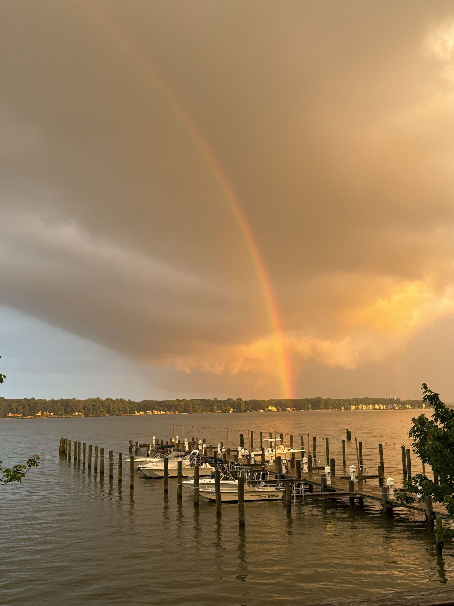 Rainbow over a calm waterfront at sunset, with a dock and moored boats in the foreground.