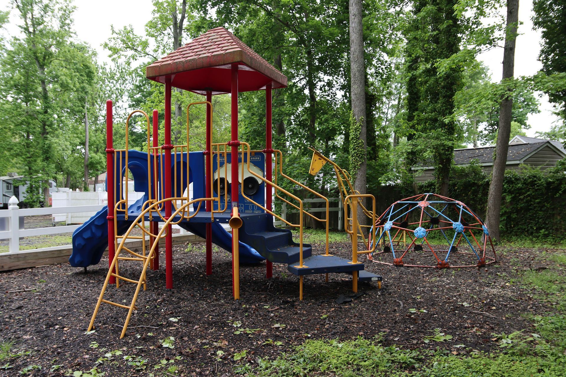 Colorful playground with slides, climbing bars, and a canopy roof in a wooded park area