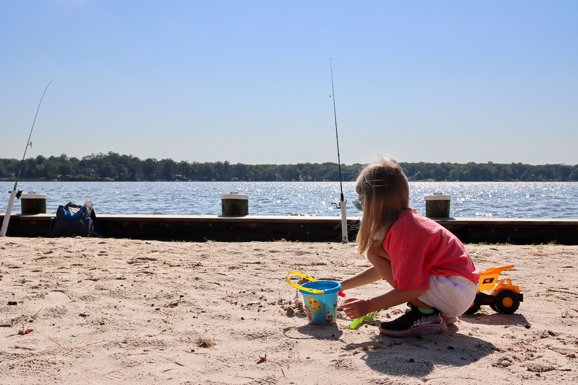 Child playing in the sand by a lake with toy buckets and a dump truck