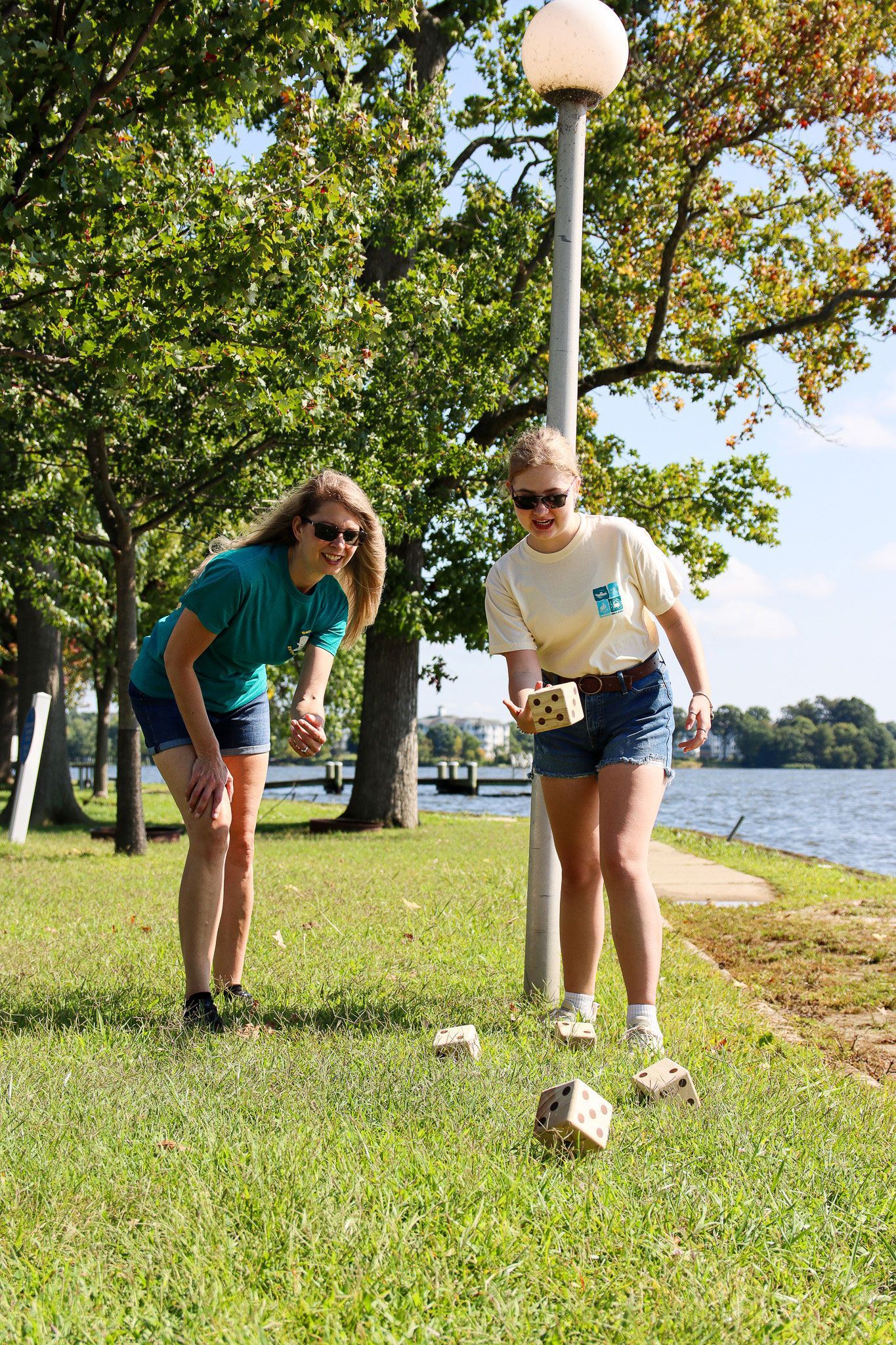 Two people playing lawn golf beside a lake under trees on a sunny day