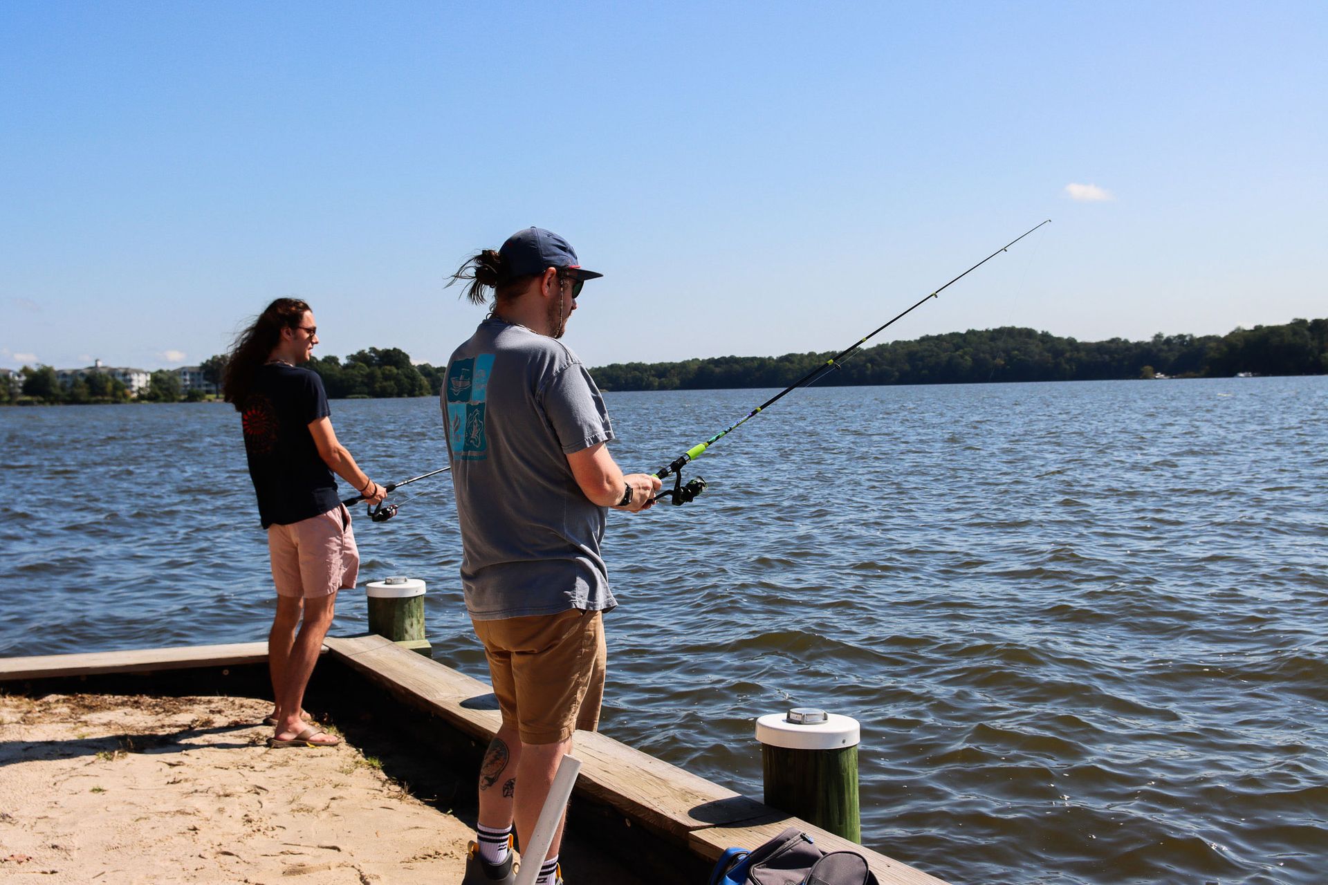 Two people fishing from a dock by a lake on a sunny day