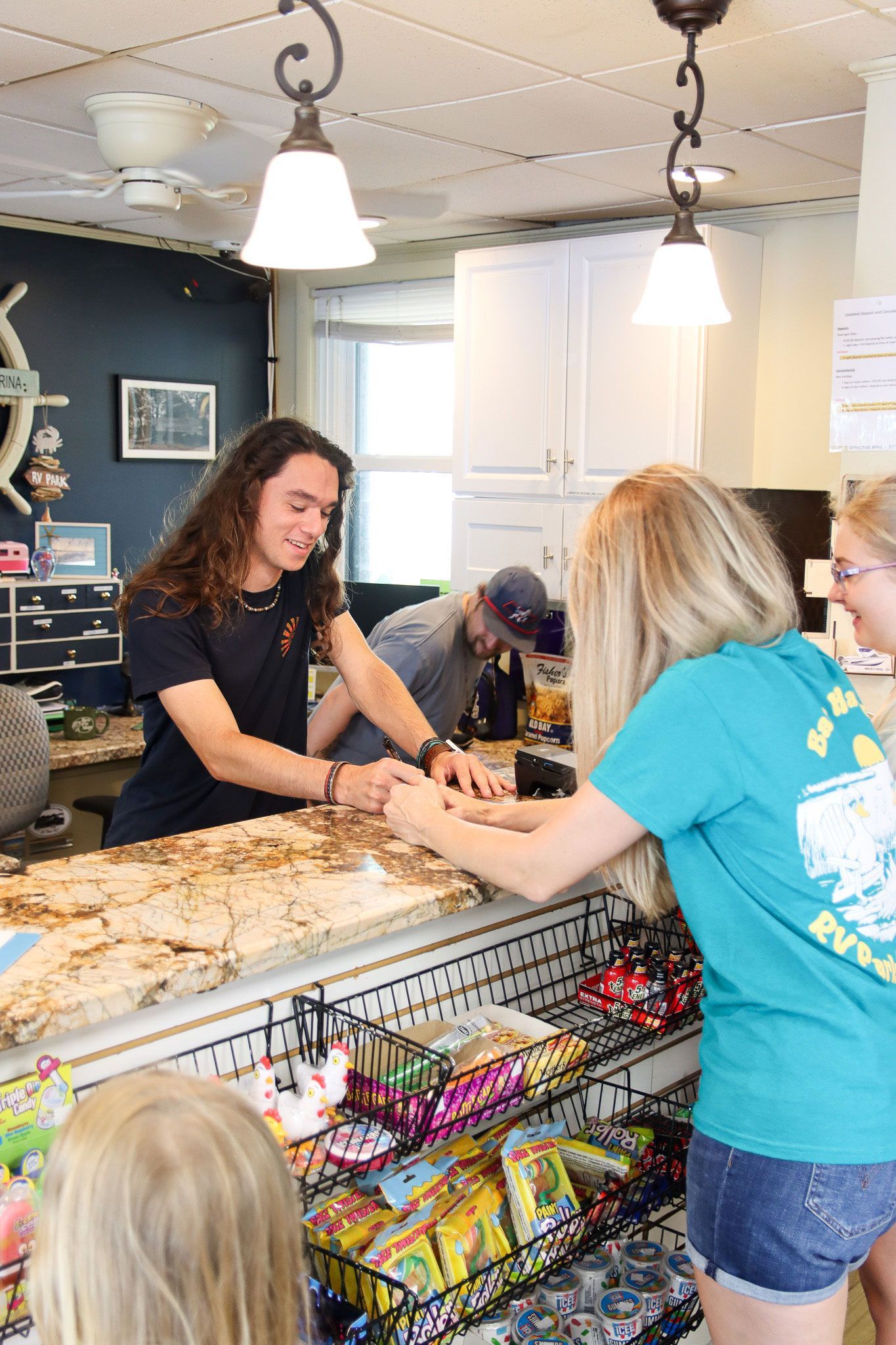 Two people talking at a shop counter with candy displays and hanging lights indoors