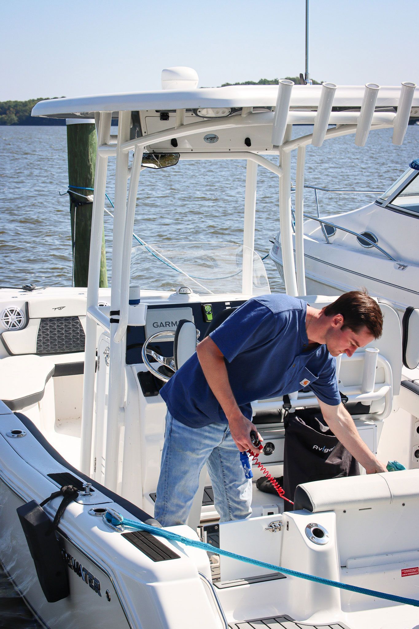 Man in blue shirt working on a boat’s deck beside fishing gear, with open water in the background