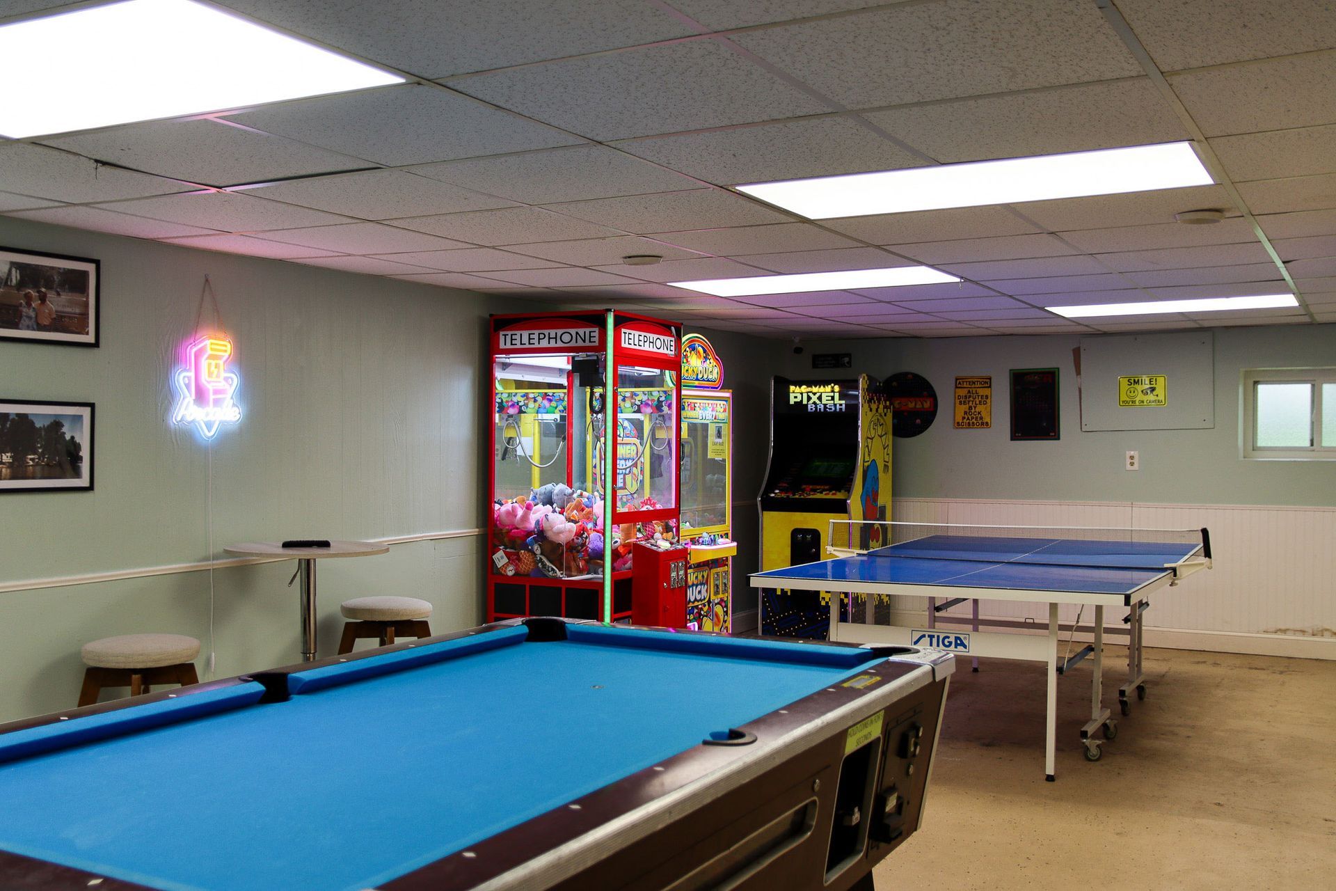 Game room with blue pool table, ping-pong table, arcade machines, and neon wall sign