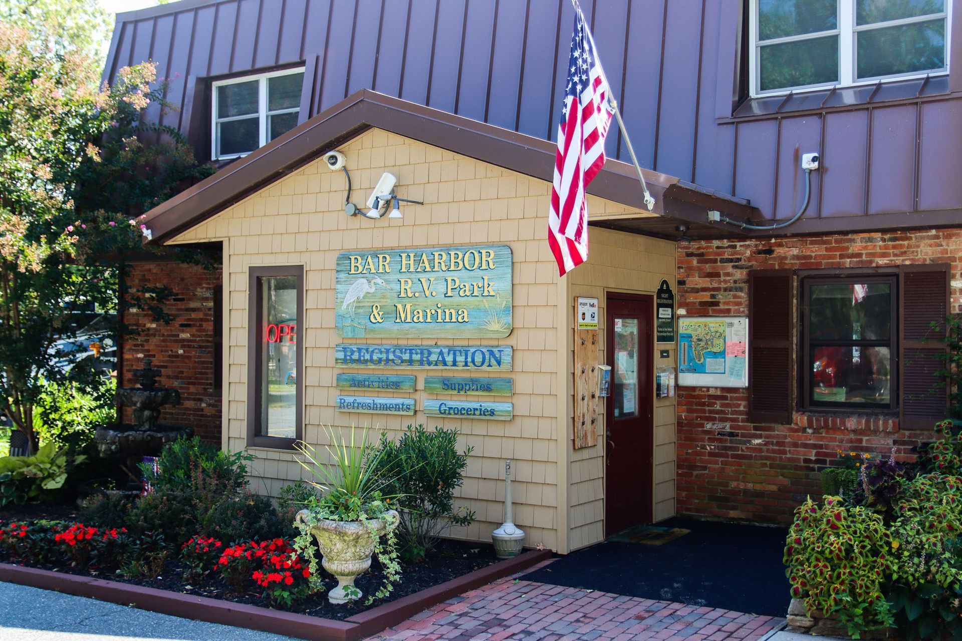 Exterior of a small office building with an American flag, brick entrance, and flower beds