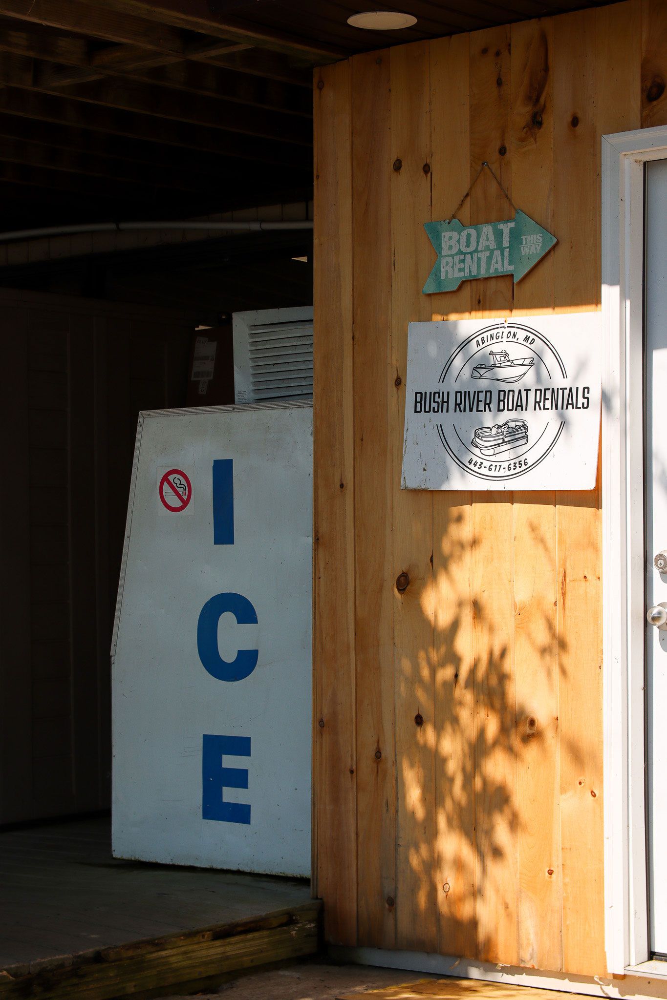 Wooden storefront with a blue and white ice machine inside, plus small wall signs by the entrance