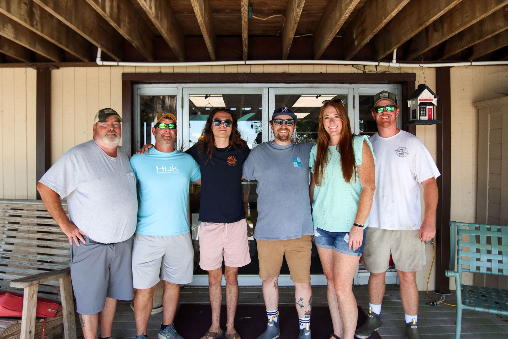 Six people standing together on a porch in front of a building, smiling at the camera.