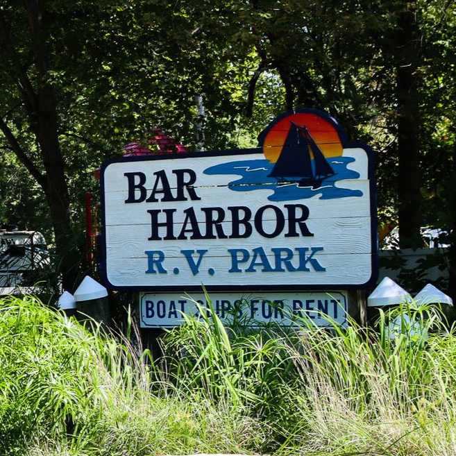 Bar Harbor RV Park sign with sailboat sunset logo and “Boat slips for rent” in a wooded setting