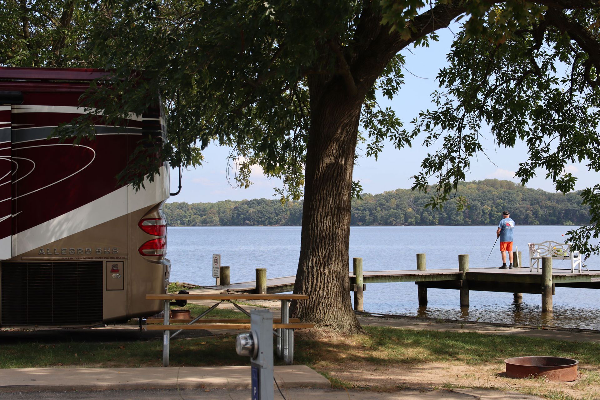 Lakeside dock with a large tree in the foreground and two people standing by the water