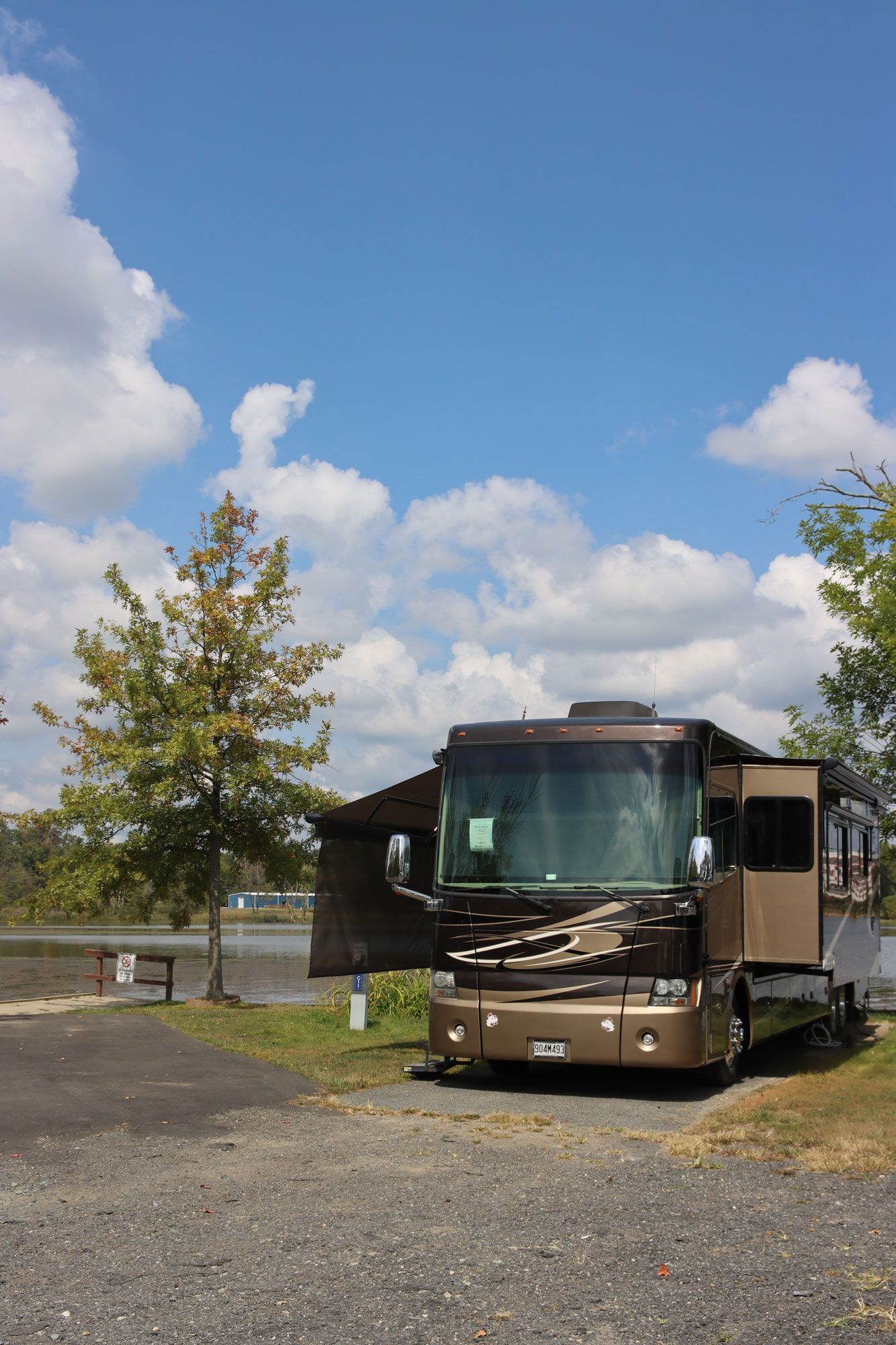 Brown RV parked on a gravel lot under a blue sky with clouds