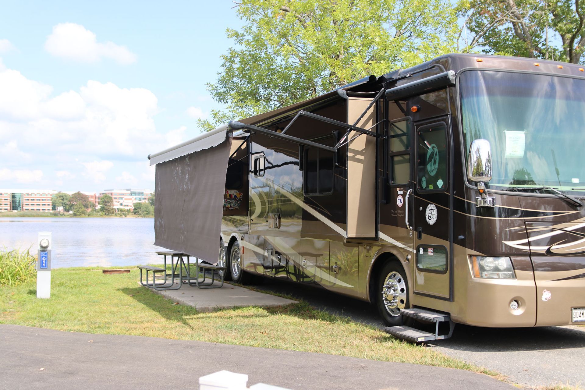 Brown RV with awning parked by a lake on a sunny day