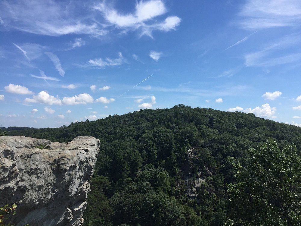 Rocky cliff overlooking a lush green hill under a blue sky with wispy clouds