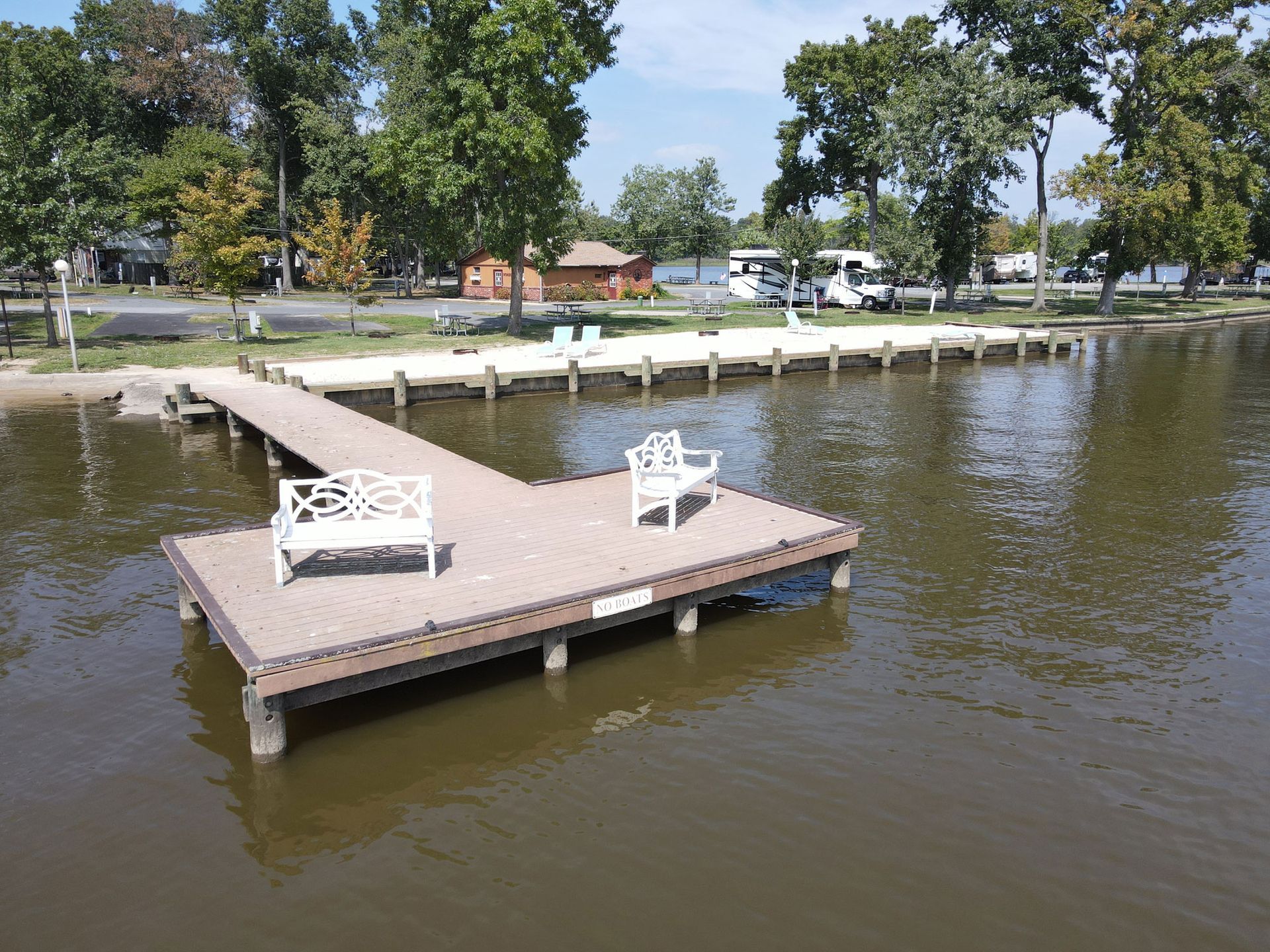 Wooden dock extending into a calm lake, with two white benches and trees along the shore.