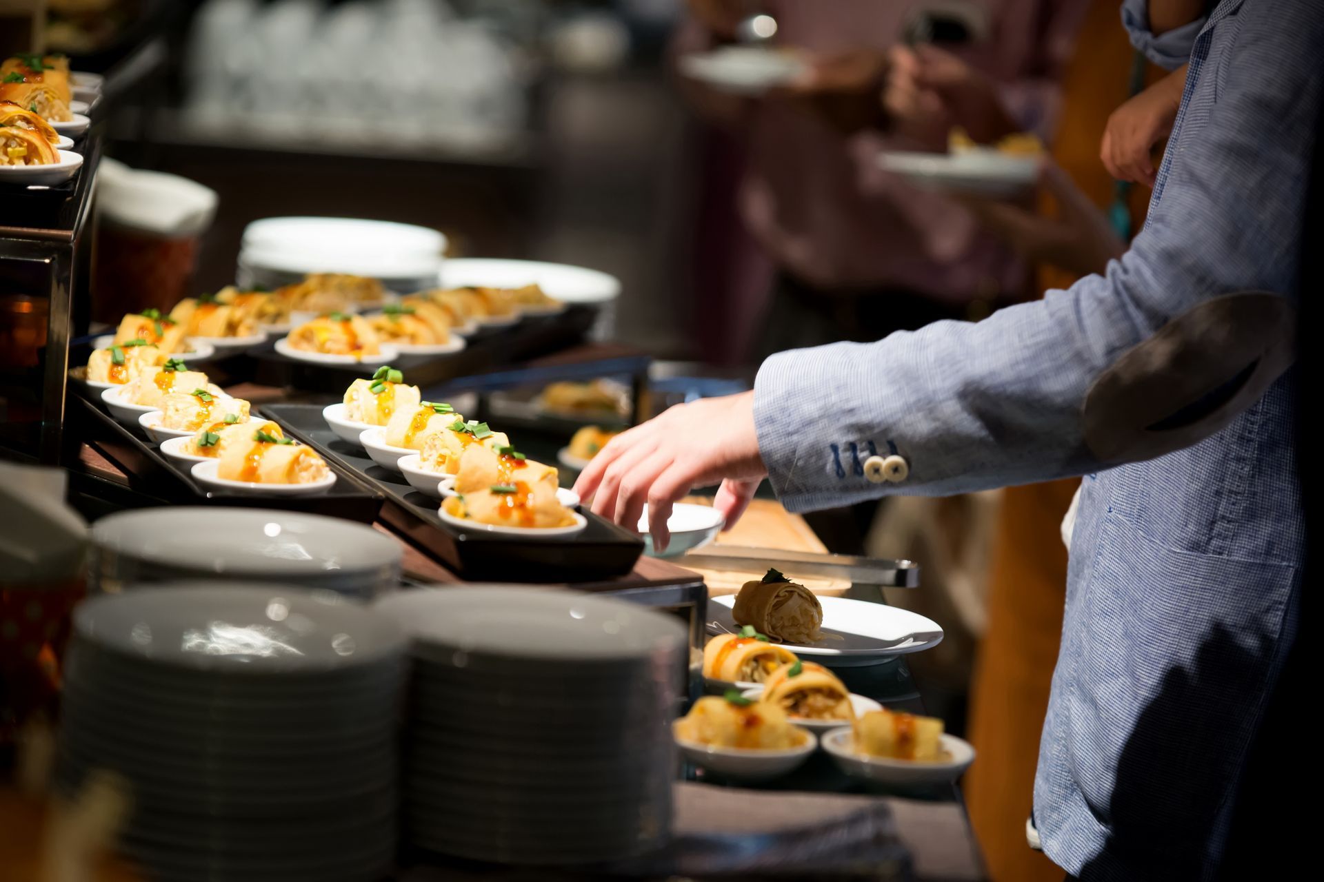 Buffet table with assorted appetizers and a hand serving food on black trays