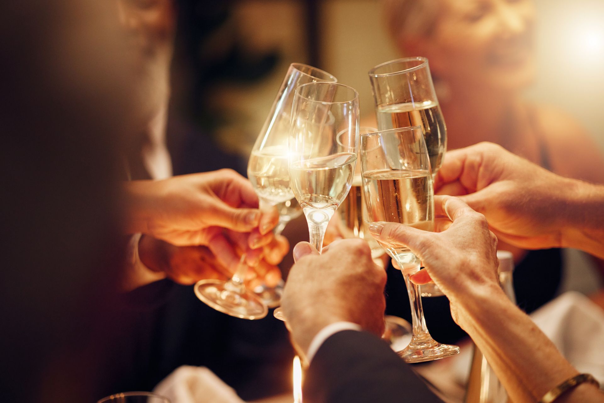 Hands raising champagne flutes in a warm-lit celebratory toast