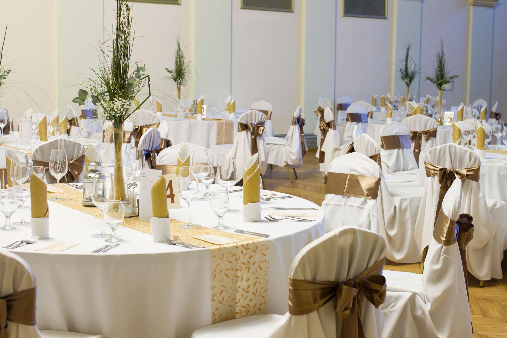 Elegant outdoor banquet tables with white tablecloths, gold accents, and flower centerpieces in a sunlit courtyard