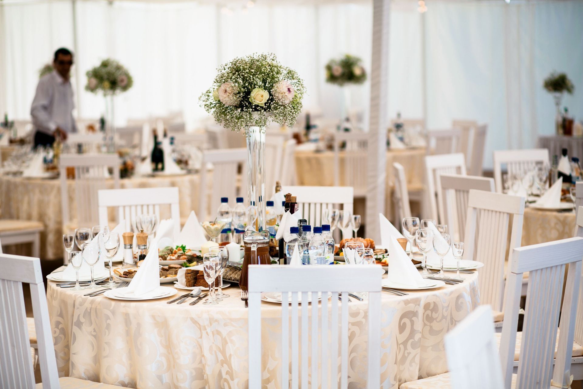 Elegant wedding reception table with white chairs, floral centerpiece, and table settings in a bright tented venue