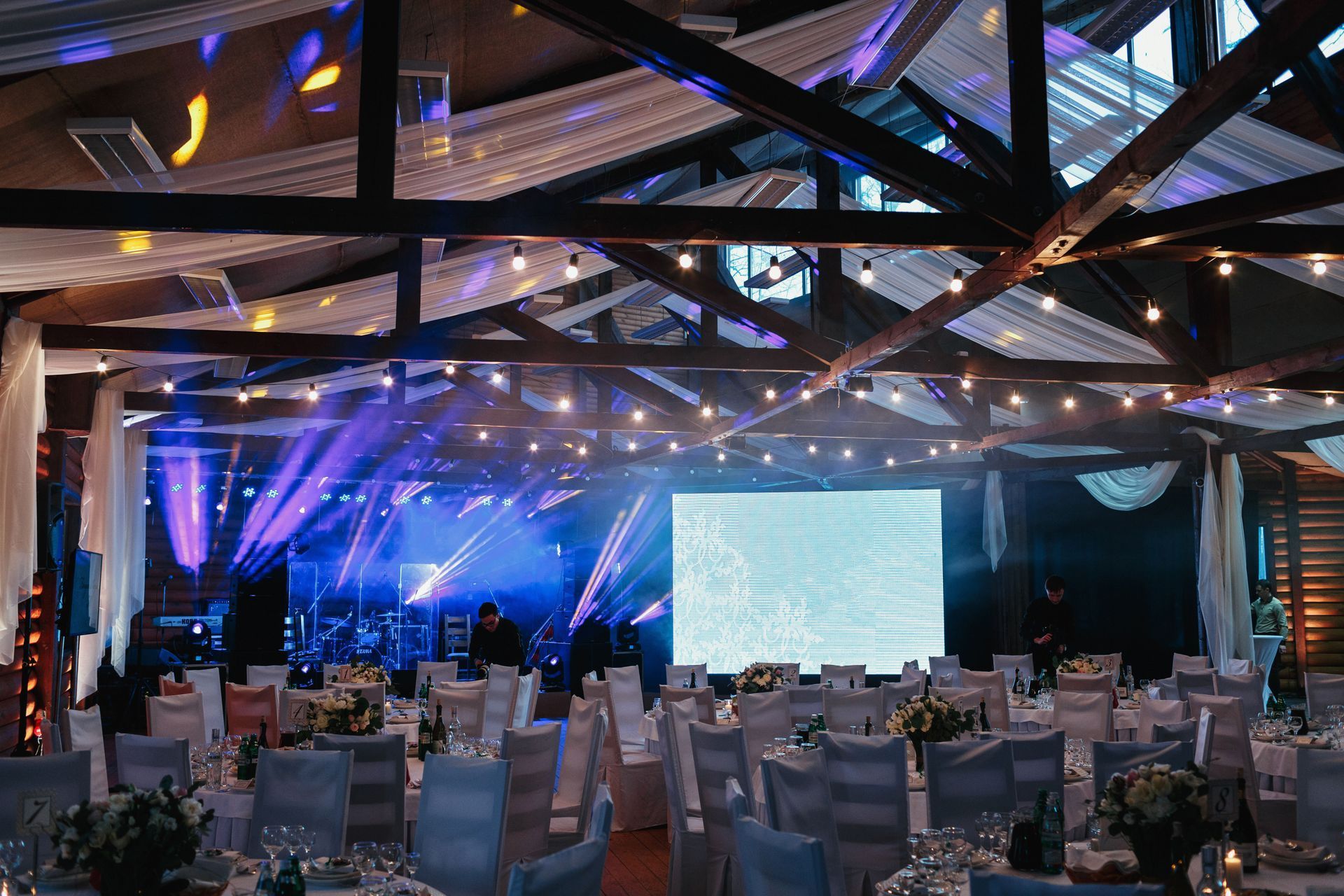 Elegant banquet hall with blue stage lighting, a large screen, and rows of empty tables and chairs