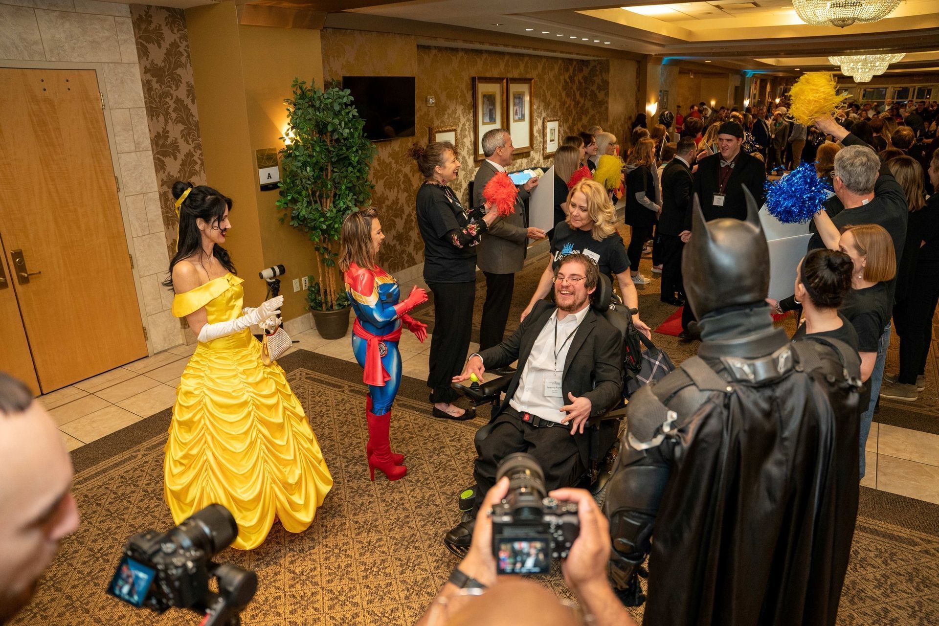Costumed crowd at an indoor convention, including Batman, Spider-Man, and a yellow ball gown character