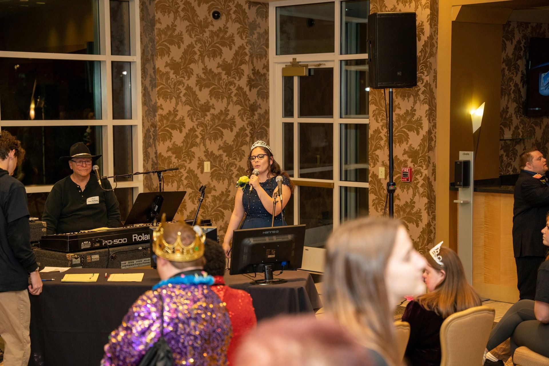 Live band performing indoors at a venue, with singer at a microphone and DJ setup beside tall windows.