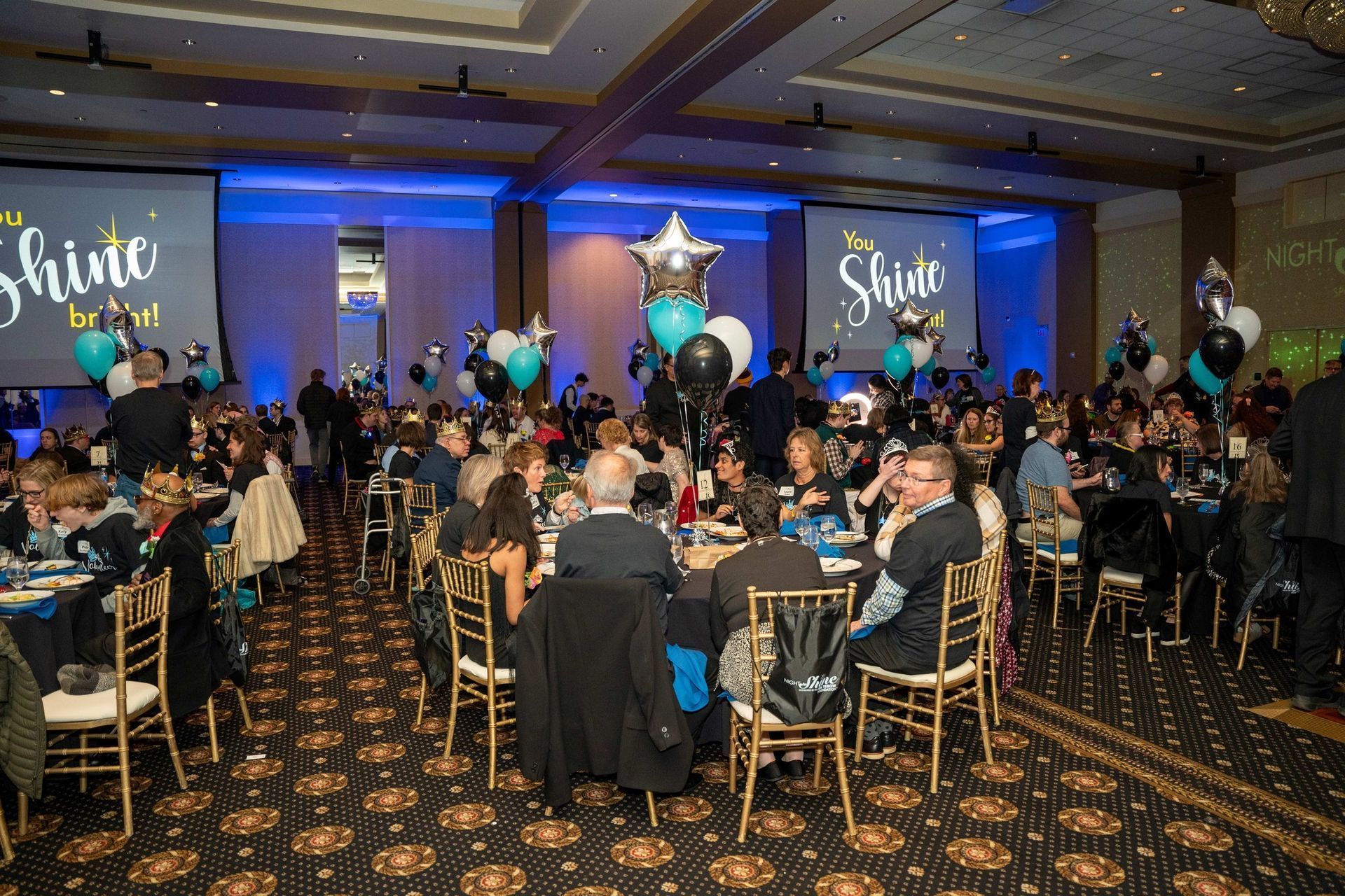 Banquet hall event with round tables, blue stage lights, and a large Shine sign on the screen
