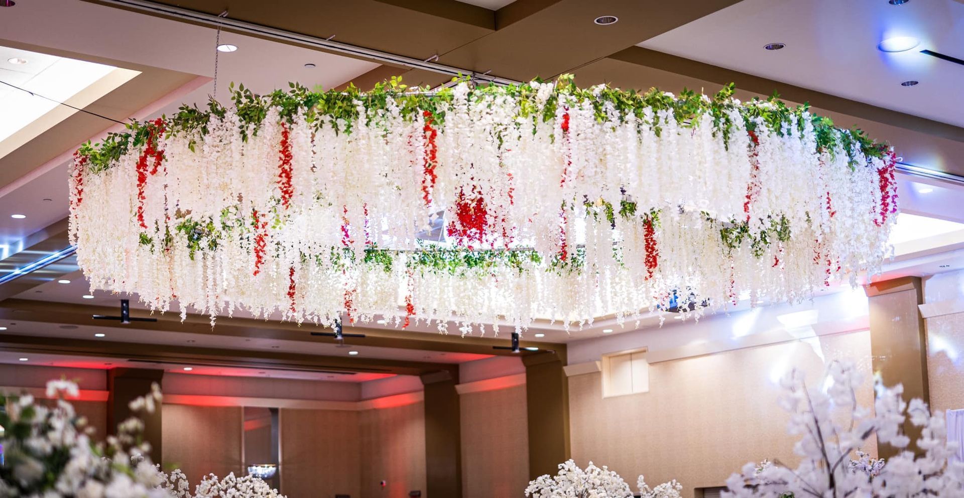 Floral ceiling installation with hanging white and red flowers in a softly lit indoor venue