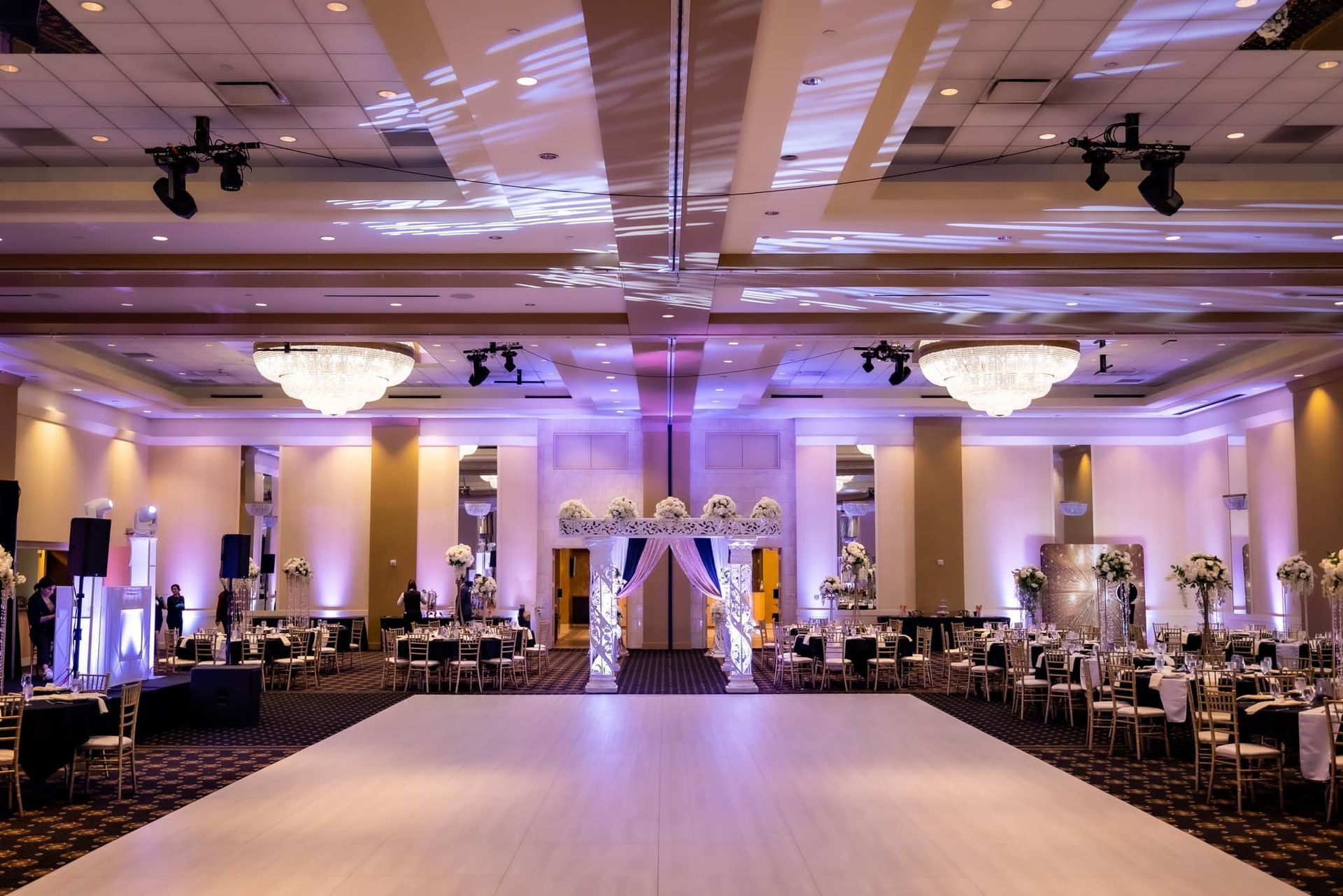 Elegant banquet hall with chandeliers, purple uplighting, and a central dance floor set for an event