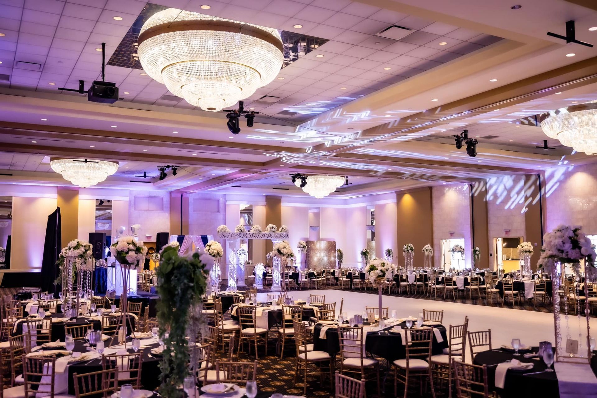 Elegant banquet hall with chandeliers, purple uplighting, and set tables for a formal event
