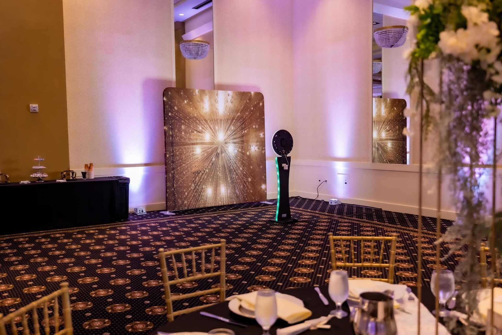 Elegant banquet hall with gold chairs, patterned carpet, and purple uplighting around a decorative stage backdrop