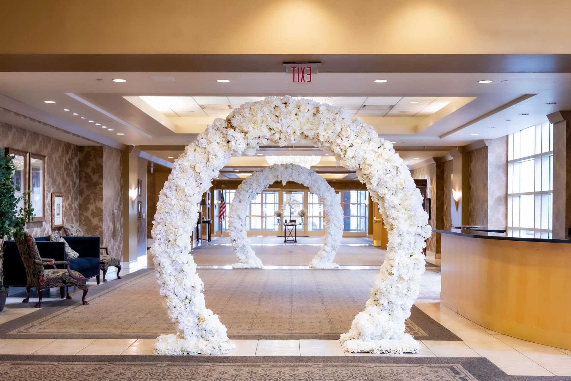 White floral arch in a hotel lobby with carpeted floor and reception desk.