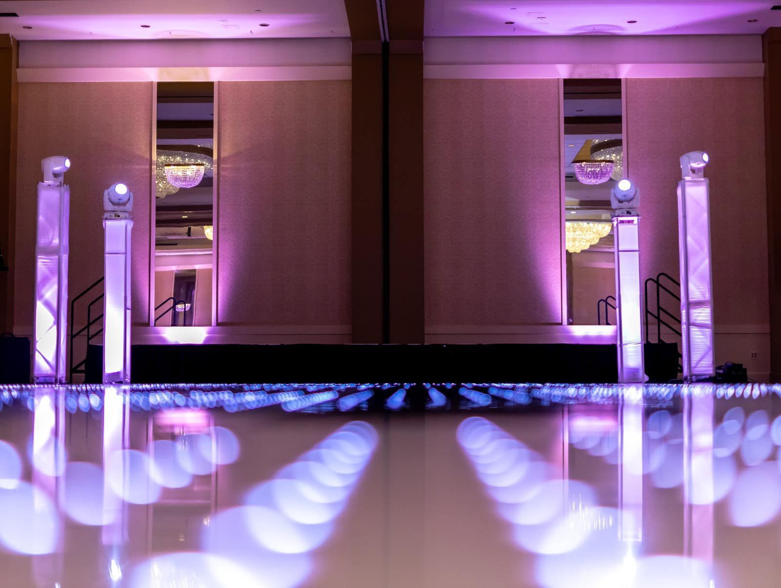 Purple-lit banquet hall with mirrored runway, glossy floor, and decorative columns