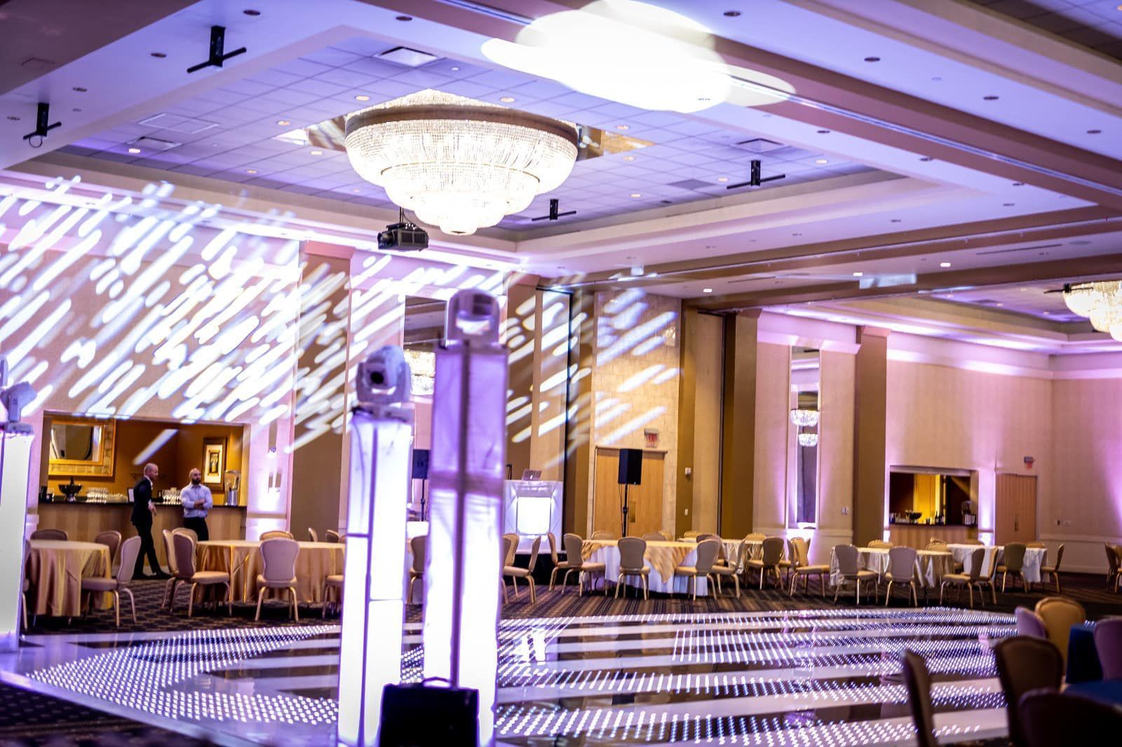Elegant banquet hall with chandeliers, round tables, and purple lighting reflections on the floor