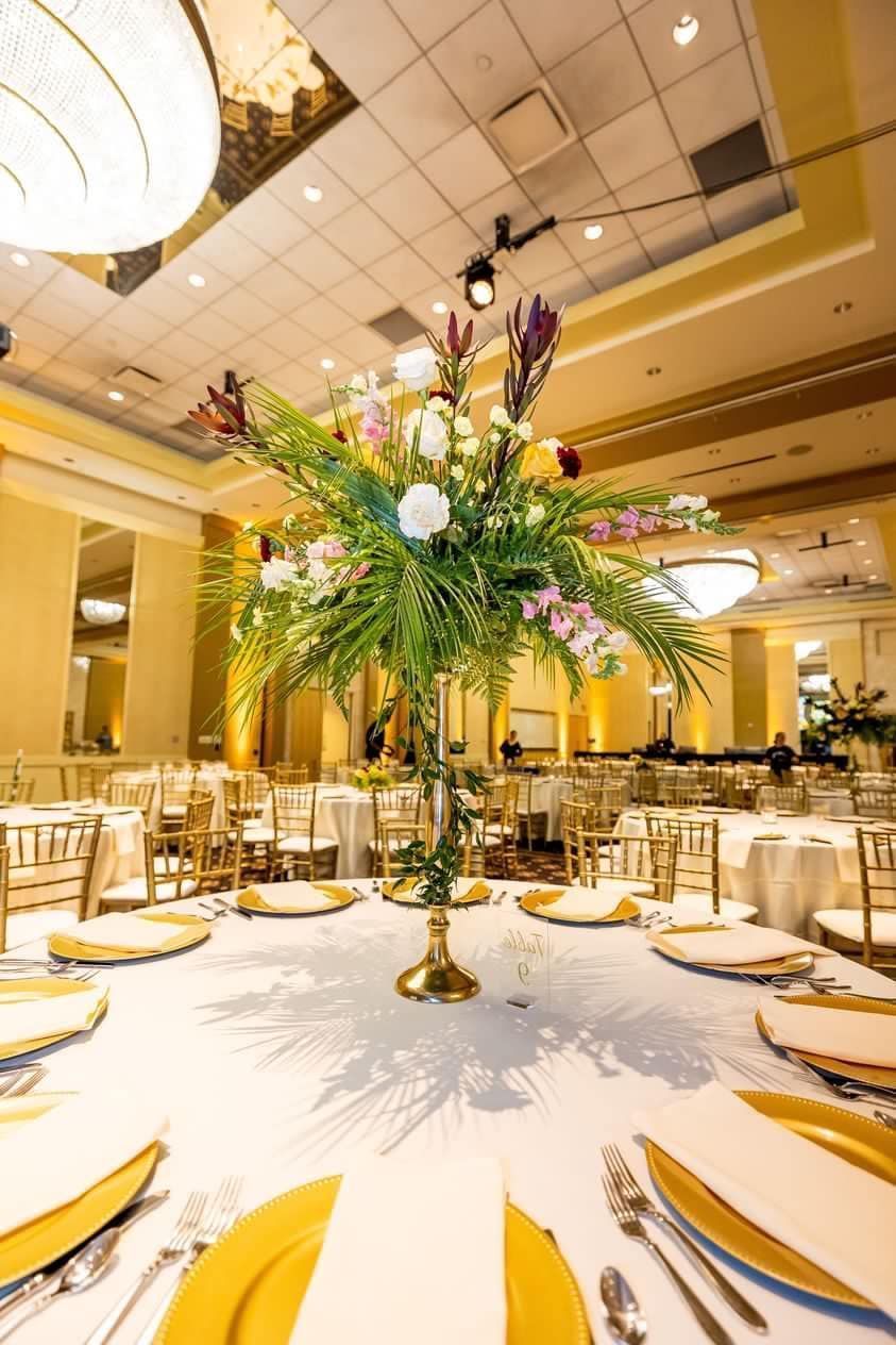 Elegant banquet table with gold accents and a tall floral centerpiece in a warmly lit ballroom